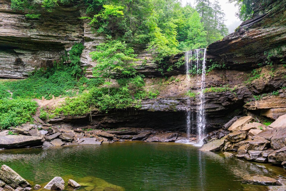 Una cascada se precipita en una piscina cristalina rodeada de riscos y abundante vegetación.