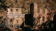 Una estructura de maó abandonada amb obertures arquejades i una xemeneia alta al bell mig d'una vessant boscosa.
