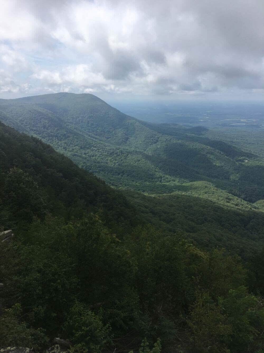 A mountainous landscape with dense green forests and a cloudy sky.