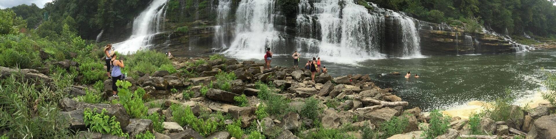 A waterfall cascading over rocks into a river surrounded by lush greenery.