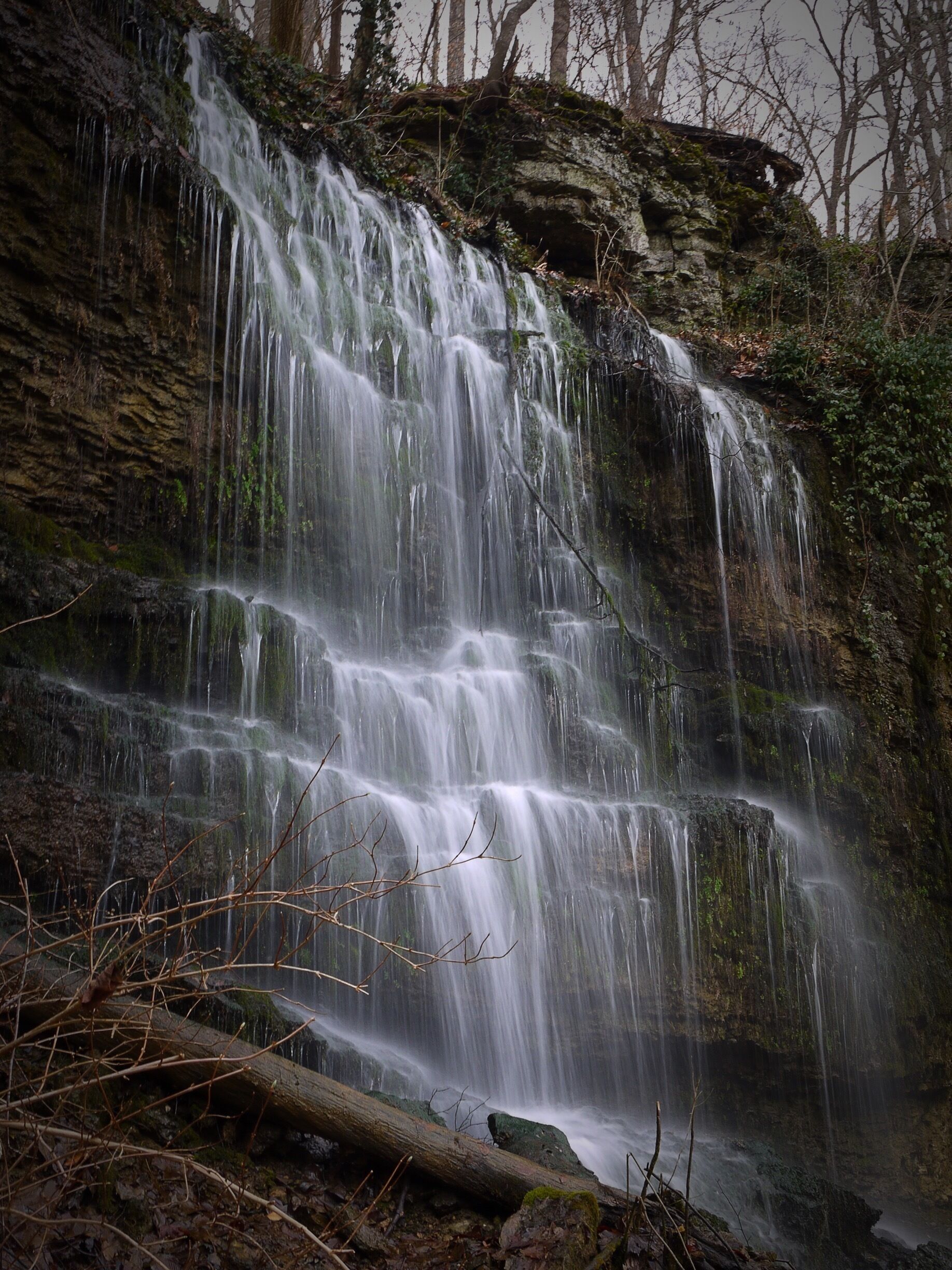 A multi-tiered waterfall cascading down a rocky cliff surrounded by trees.