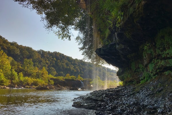 Ein Fluss fließt durch ein bewaldetes Tal, an einer Seite befindet sich eine felsige Klippe.
