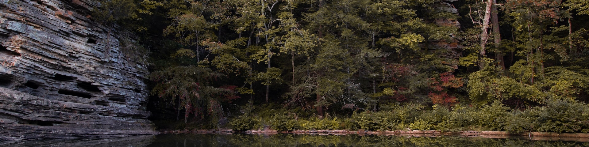 Ein felsiger Klippenhang, dichter Wald und ein stiller See.