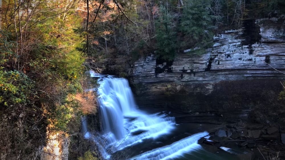 Une cascade d’eau se déversant sur une falaise rocheuse, le tout étant entouré d’arbres.