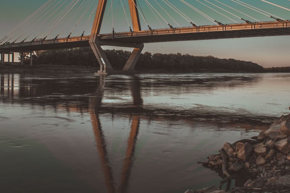 A cable-stayed bridge over a river with a rocky shoreline in the foreground.