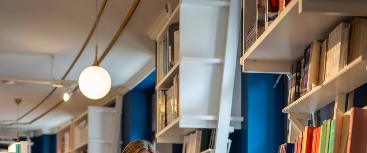 Enthusiastic woman selects books in bookstore alone. Female book lover browsing, searching textbooks, handbooks, library visit, book fair, book crossing, literature passion, bibliophile in store