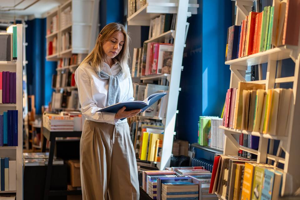 Una persona leyendo un libro en una librería con pisos de madera y estanterías blancas.