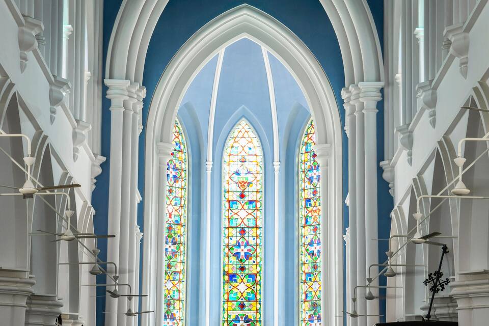 Interno di una chiesa con soffitto a volta alto, vetrate colorate e banche.