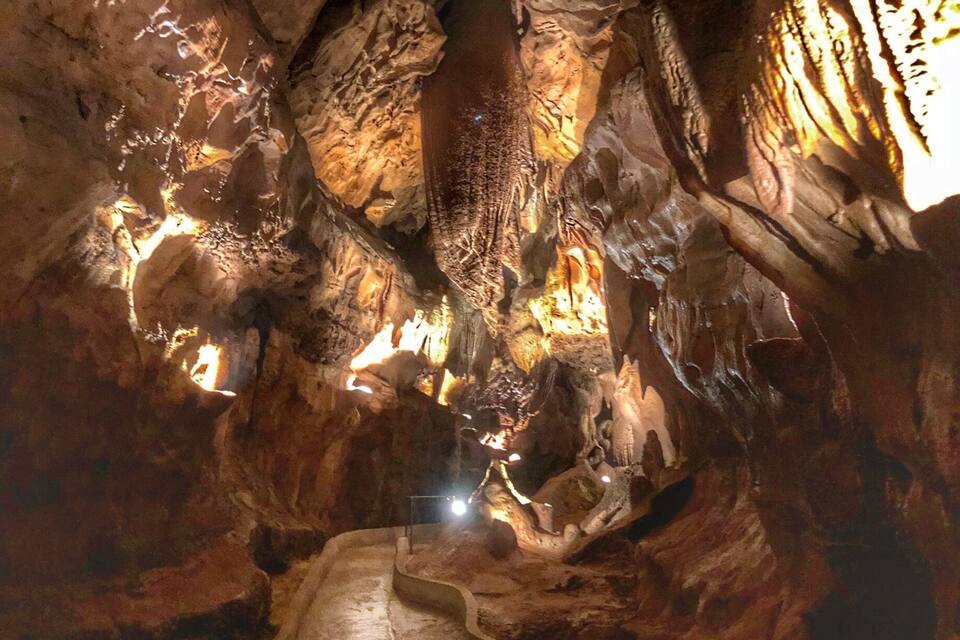 A cave with stalactites and stalagmites, a narrow passage, and a light source illuminating the formations.