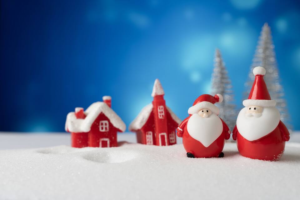 Dues figures de Pare Noel, una casa vermella i un paisatge cobert de neu amb cel blau.
