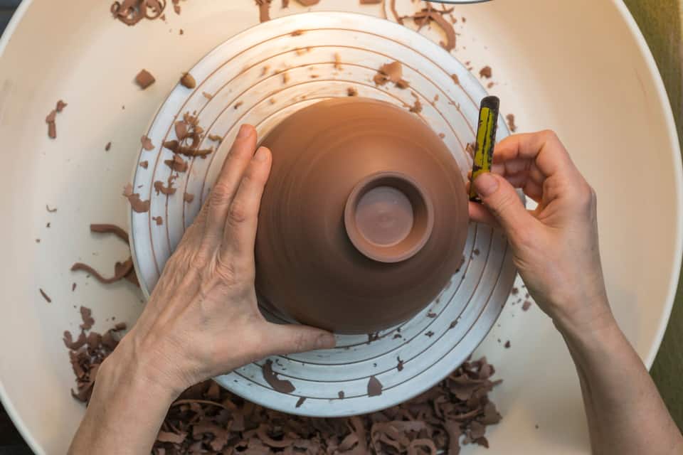 A person shaping a clay pot on a spinning wheel.