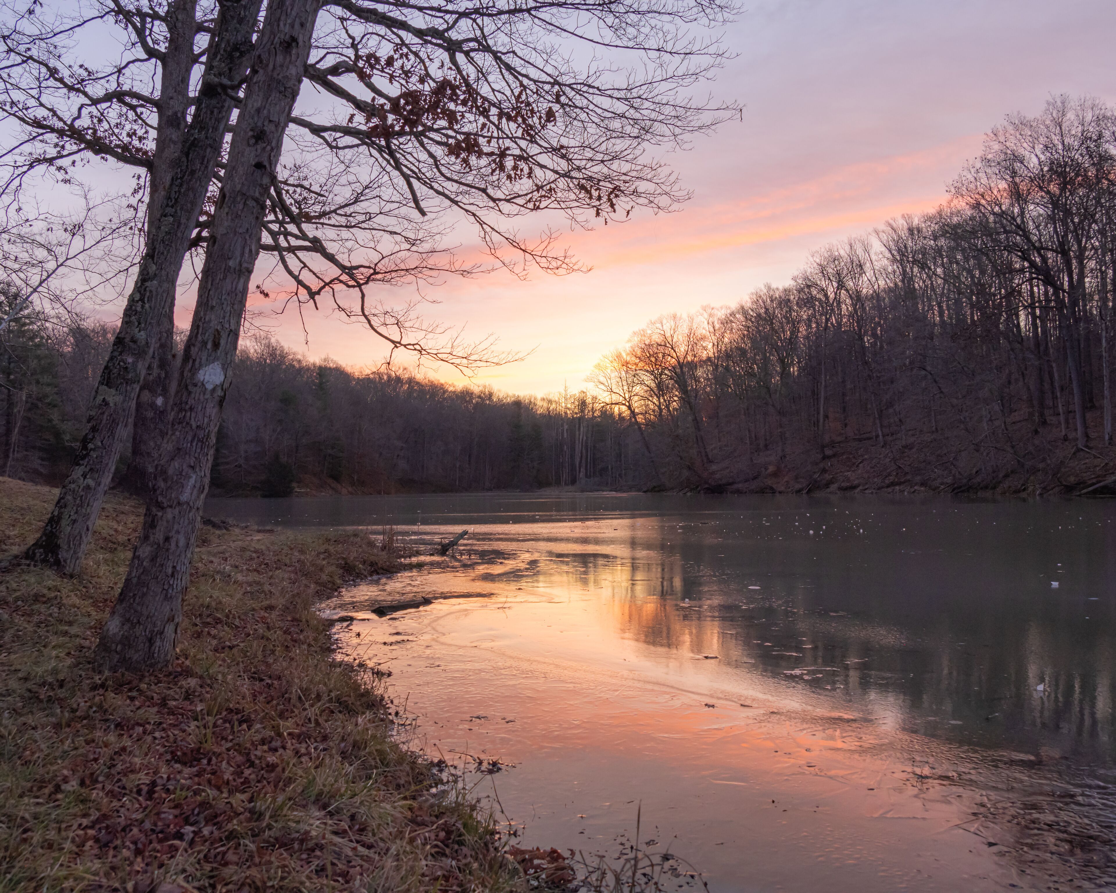 Early morning sunrise over a small lake covered in ice during the winter in Indiana. The sky is orange, yellow, purple and blue. 