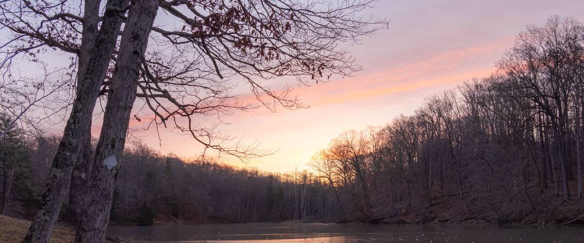 Early morning sunrise over a small lake covered in ice during the winter in Indiana. The sky is orange, yellow, purple and blue.