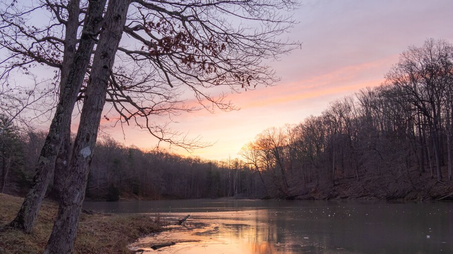 Early morning sunrise over a small lake covered in ice during the winter in Indiana. The sky is orange, yellow, purple and blue.