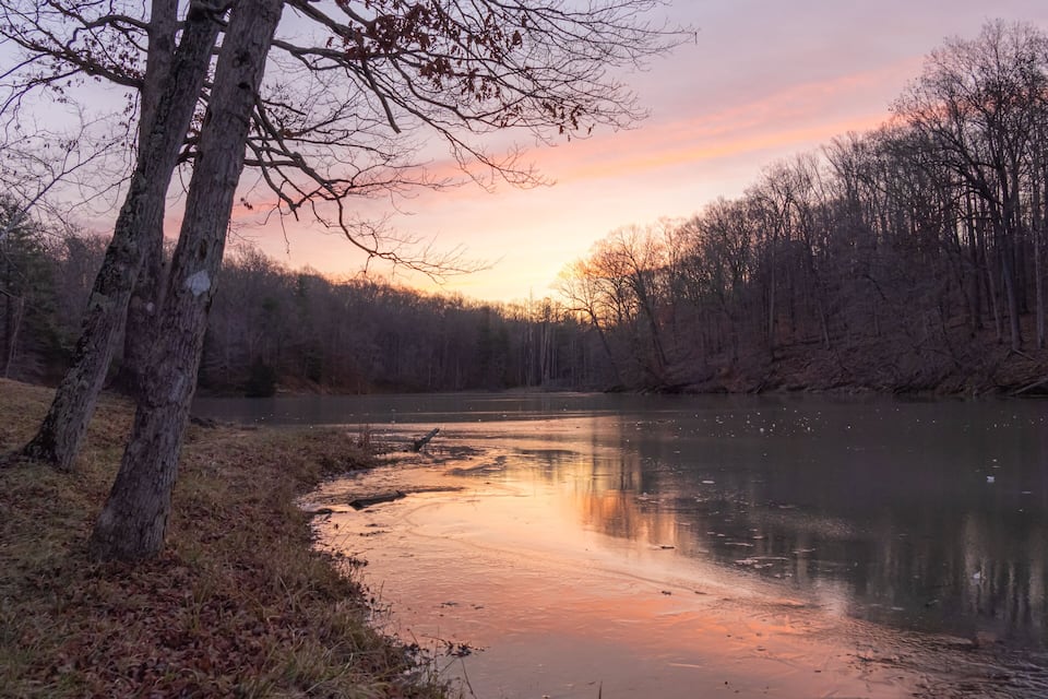 A calm river at sunset with trees reflecting the sky.