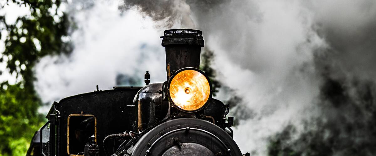 Vintage museum steam train approaching through green forest.