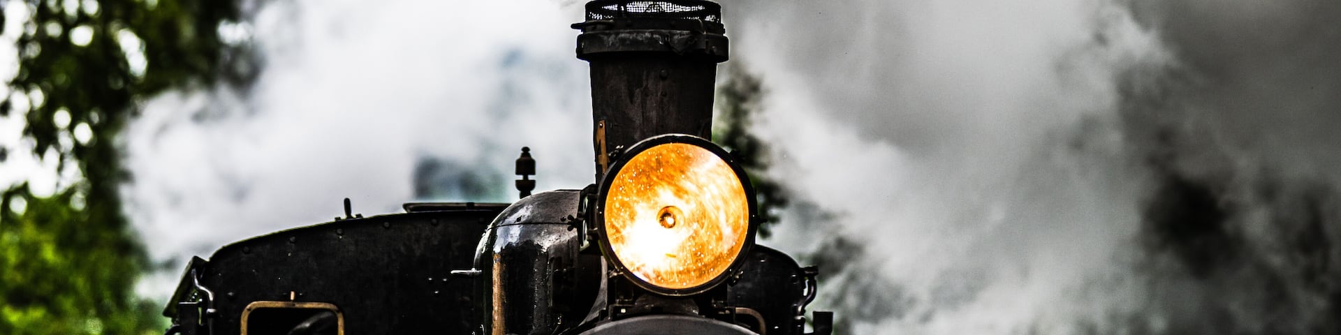Vintage museum steam train approaching through green forest.