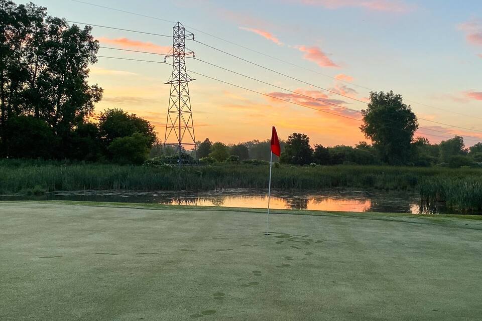 A sunset over a water body with a power line tower and a flagpole in the foreground.