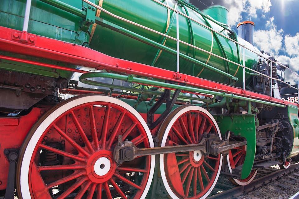 A green steam locomotive with red wheels and a white center, featuring a large boiler and multiple connecting rods.