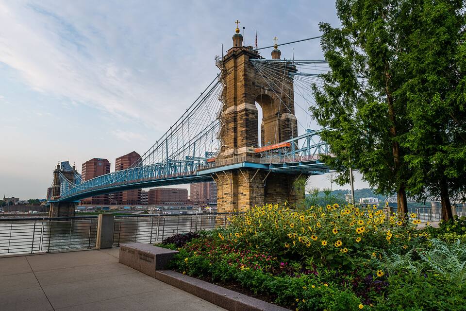 Een hangbrug met een stenen toren, een rivier en een bloementuin.