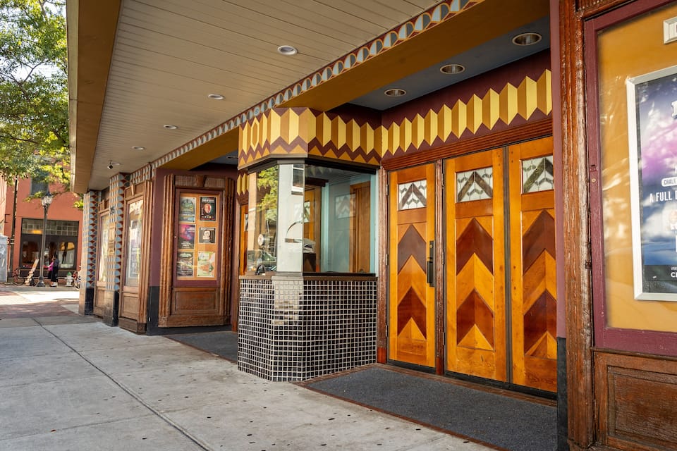 Een theater met een 'Binnenkort' bord, een affiche voor 'CBS Sports HQ House' en een decoratief gevelontwerp.