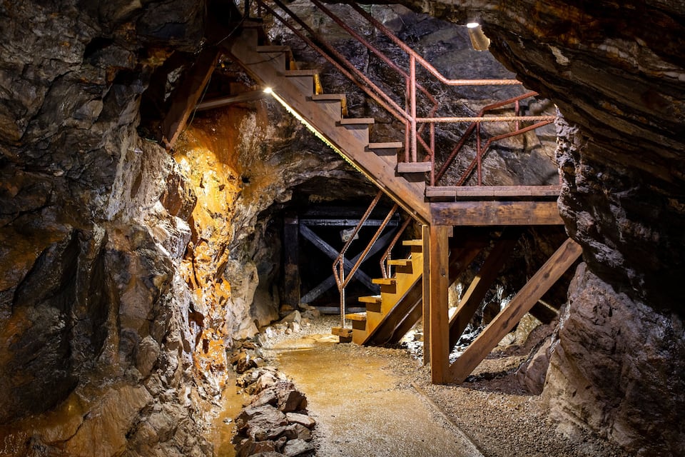 Un escalier en bois dans un tunnel rocheux, avec des rampes en métal.