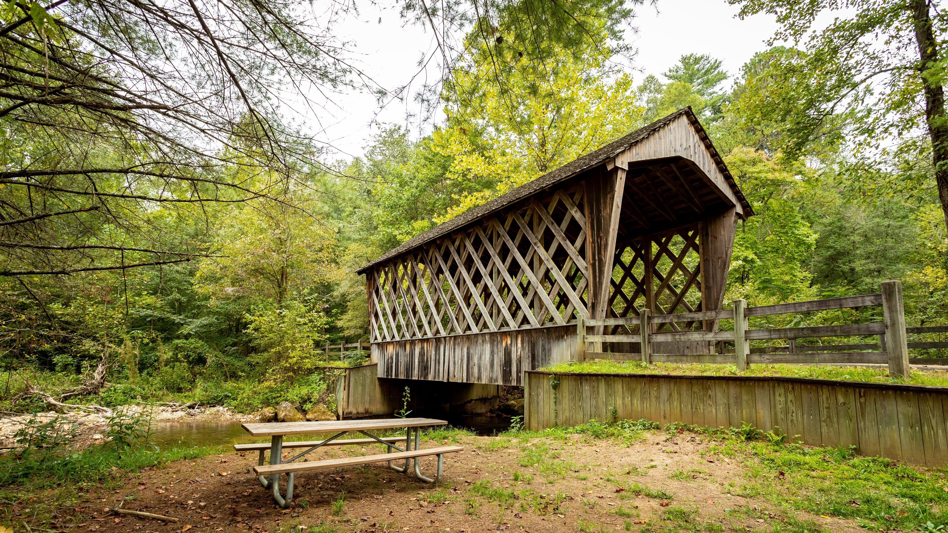 A wooden covered bridge with a picnic table in a forested area.