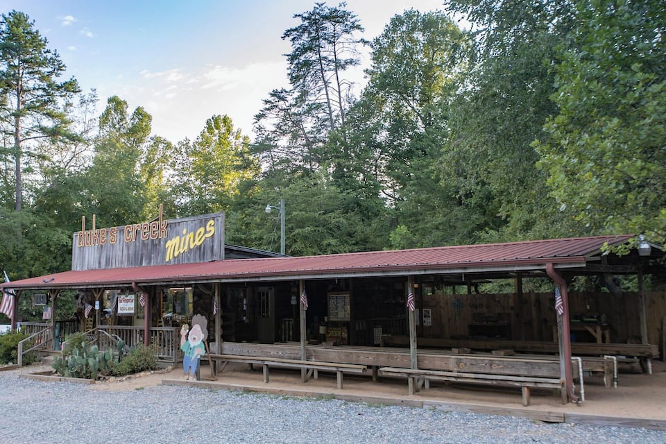 A rustic building named 'Duke's Creek Mines' with a wooden exterior and a red roof, surrounded by lush greenery.