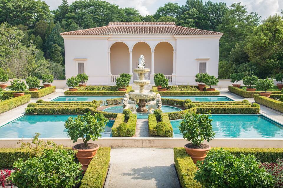 A classical garden with a fountain, geometrically trimmed hedges, and a pool.