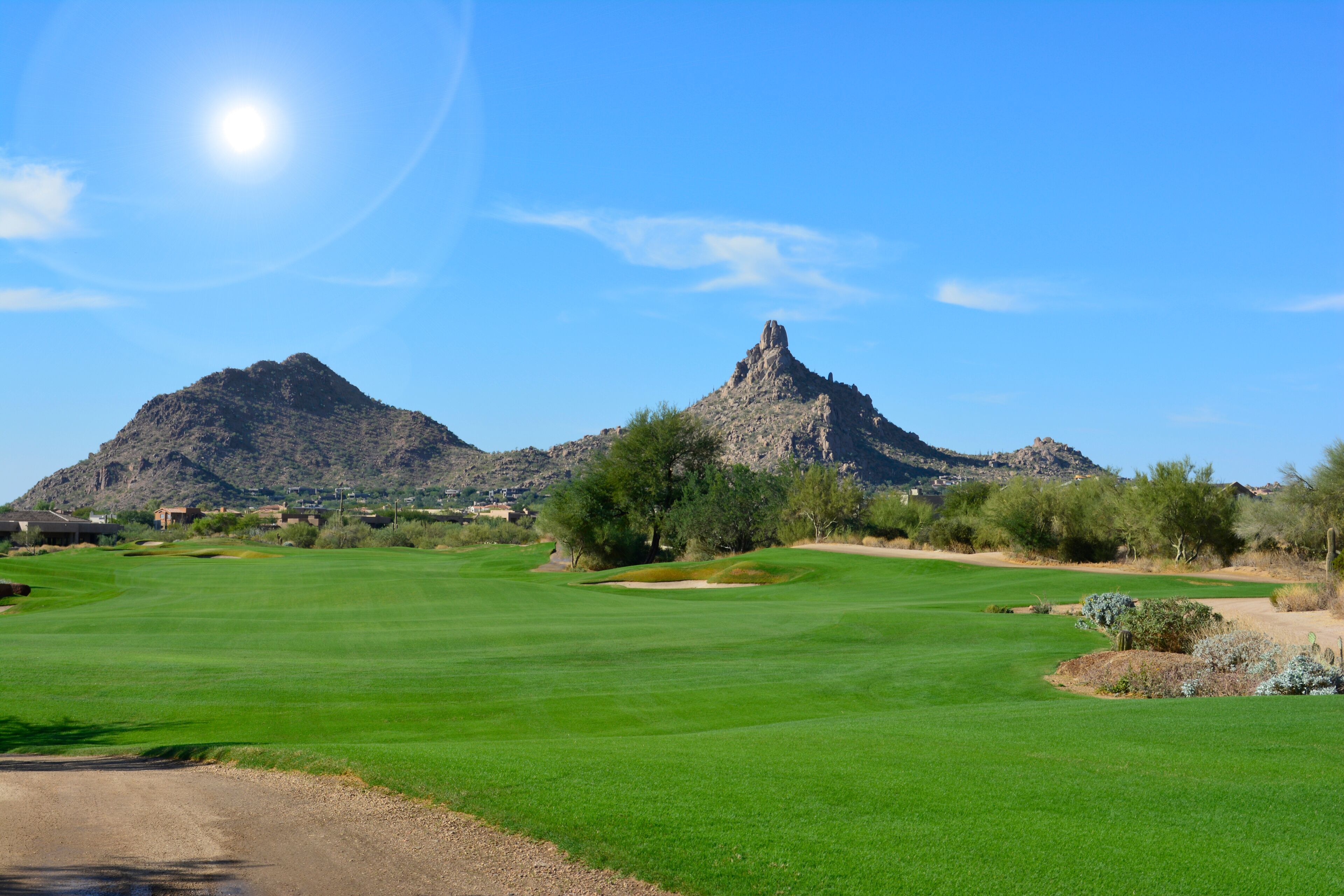 Sun shining over a green golf fairway with mountains and a blue sky