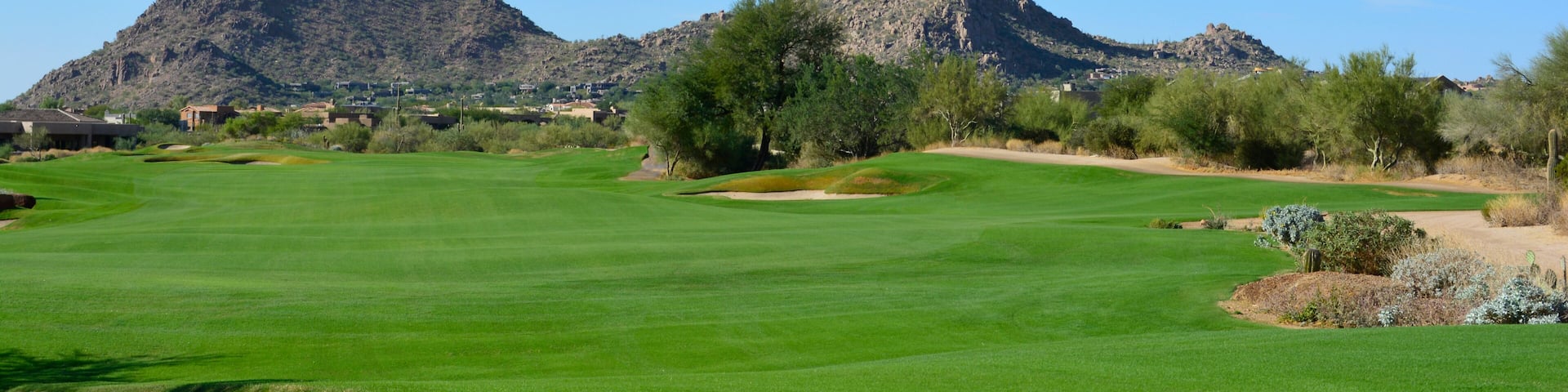 Sun shining over a green golf fairway with mountains and a blue sky