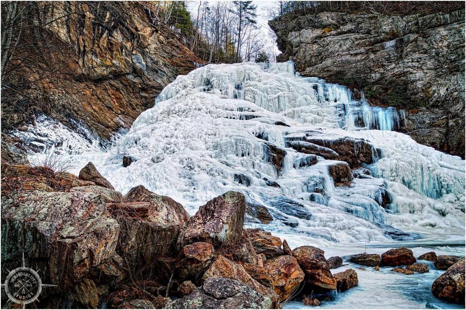 Une cascade gelée, entourée d’un paysage rocheux et d’une végétation clairsemée.