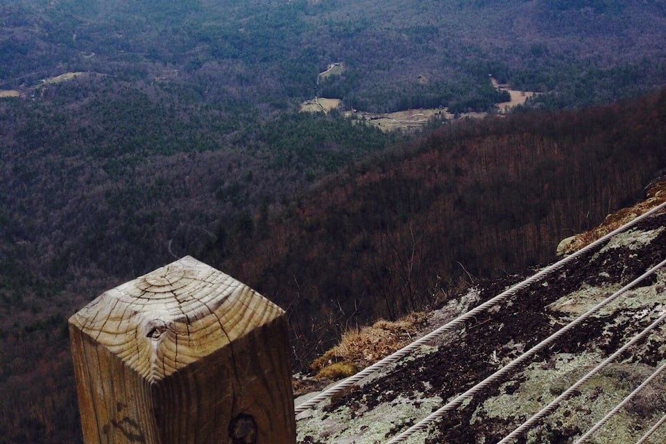 A forested mountain landscape with a wooden post in the foreground and a railway track.