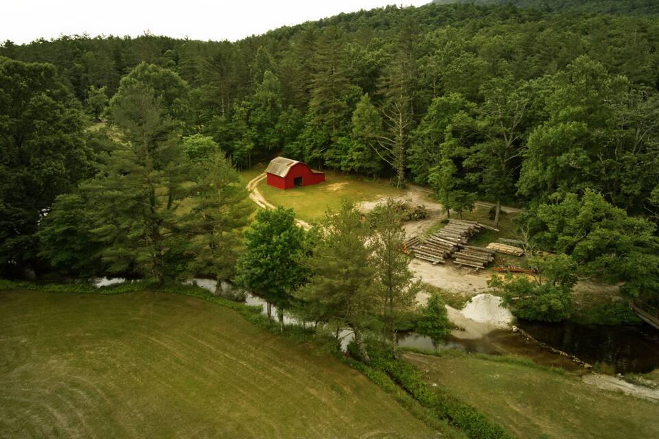 A red barn surrounded by dense forest and a river.