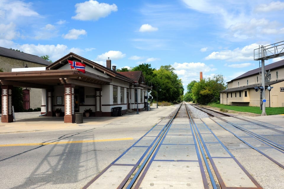 A train station with a Norwegian flag, tracks, and buildings.