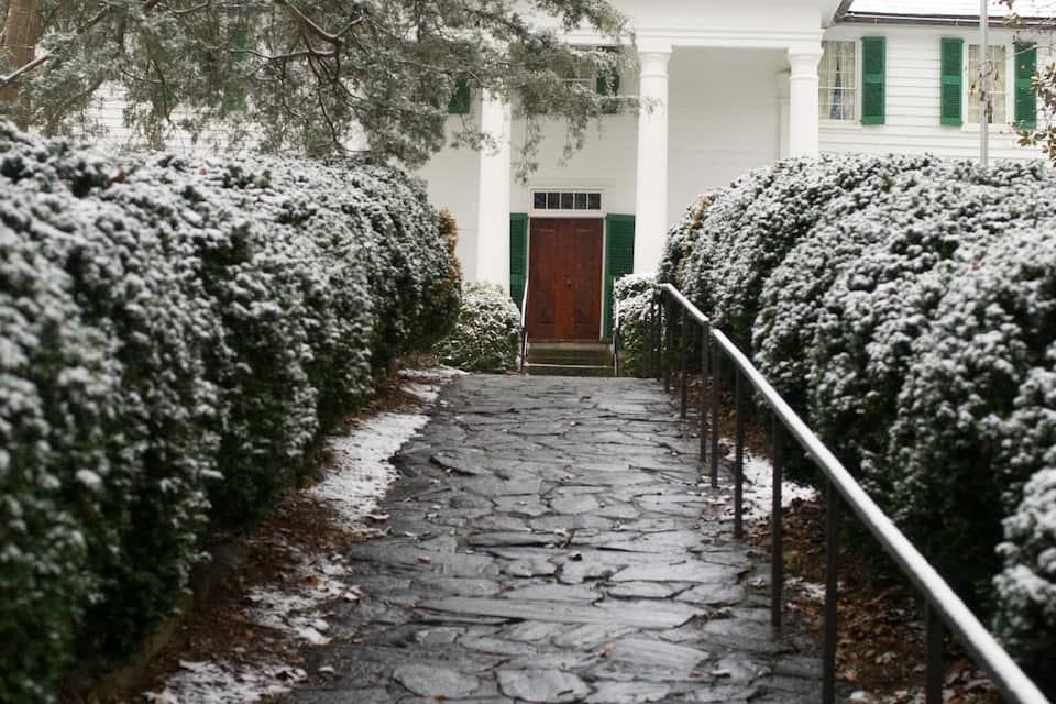 A snow-covered stone pathway leading to a white building with green shutters.