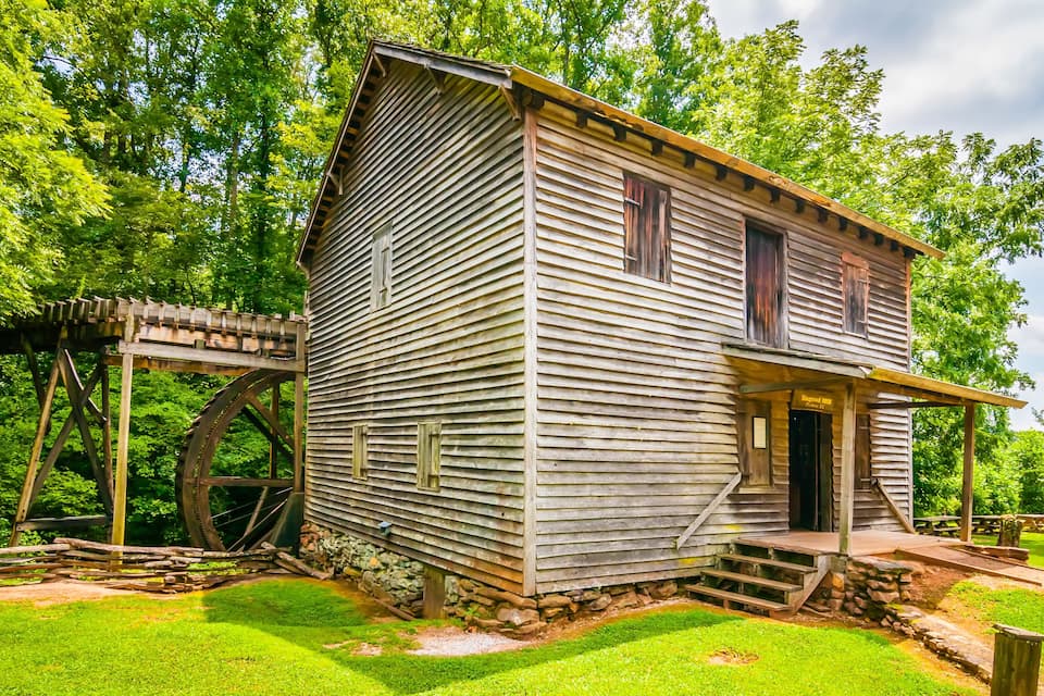 Un edificio de madera histórico con una rueda hidráulica y un porche cubierto.