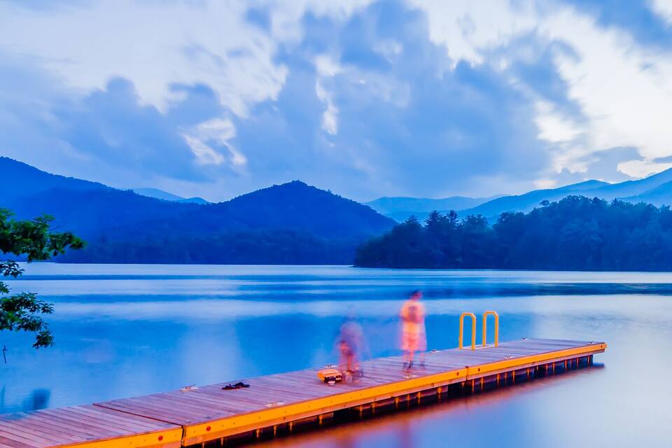 A wooden dock extending into a calm lake with mountains in the background.
