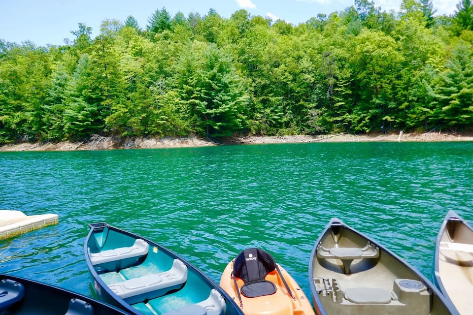 Une rangée de canoës était amarrée au bord d’un lac paisible, avec une forêt dense en arrière-plan.