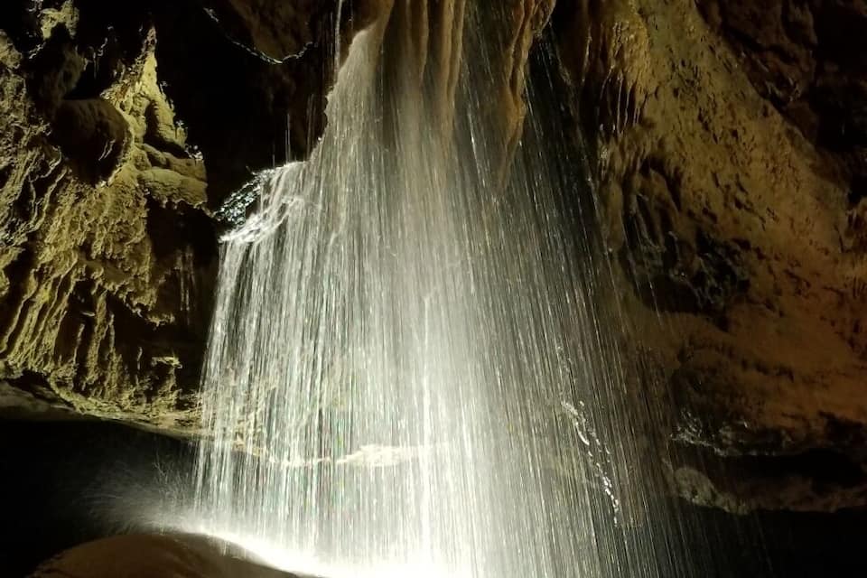 A waterfall in a cave with illuminated water.
