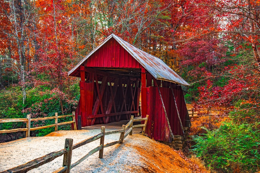 A red covered bridge in a forest with autumn foliage.
