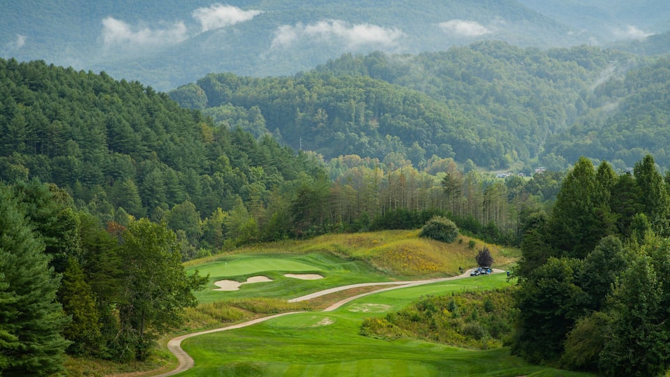 A golf course surrounded by dense forest and mountains.