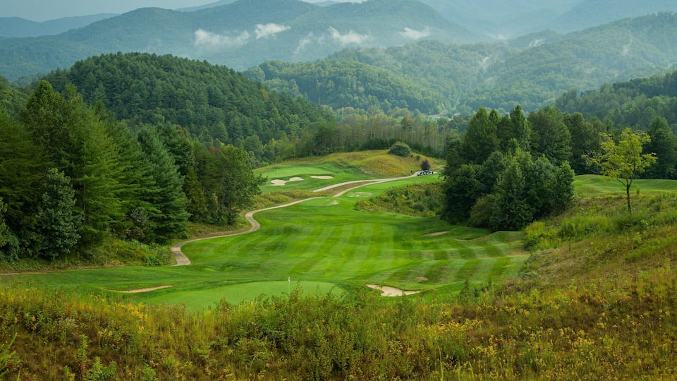 A lush green golf course surrounded by dense forests and rolling hills.