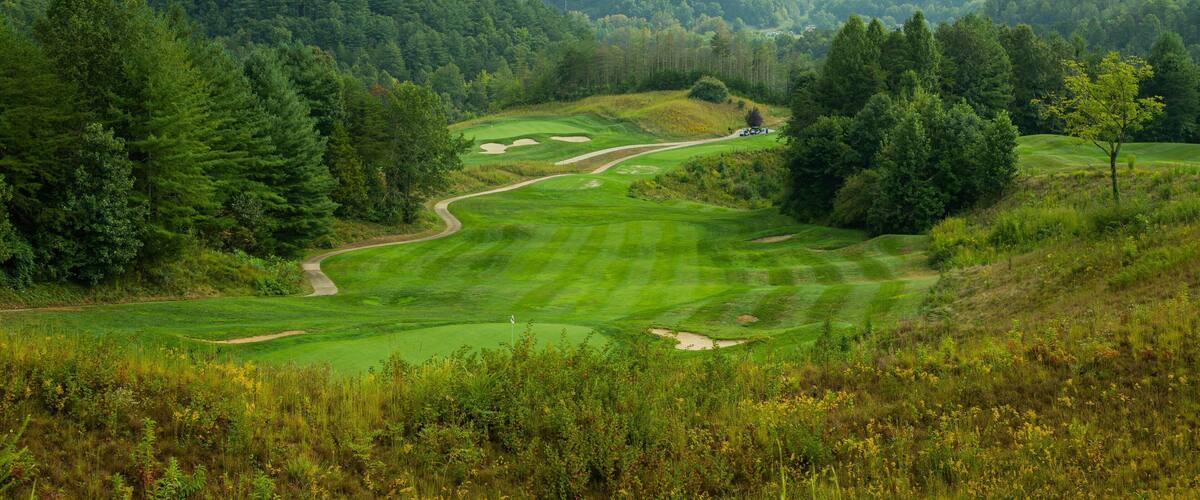 A lush green golf course surrounded by dense forests and rolling hills.