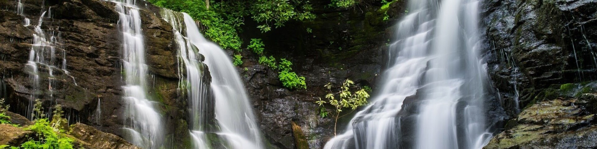 Uma cascata descendo sobre pedras em uma área arborizada.