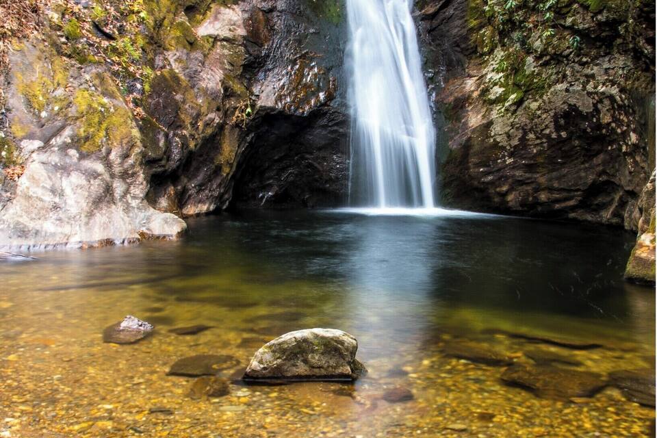 A waterfall cascading into a clear pool surrounded by rocky terrain and greenery.