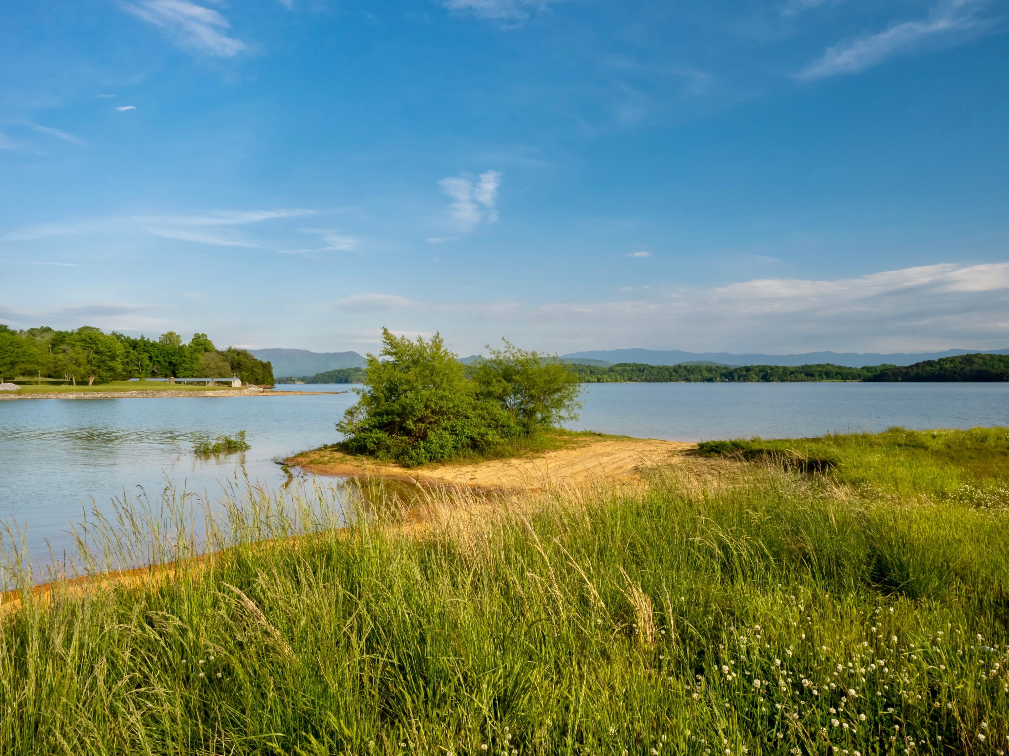 Douglas Lake in the spring in Tennessee with the Great Smoky Mountains in the background, the water and sandy shore with a blue sky filled with clouds in the distance.