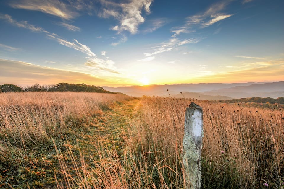 Een zonsondergang boven een grasveld, met een houten paal op de voorgrond.