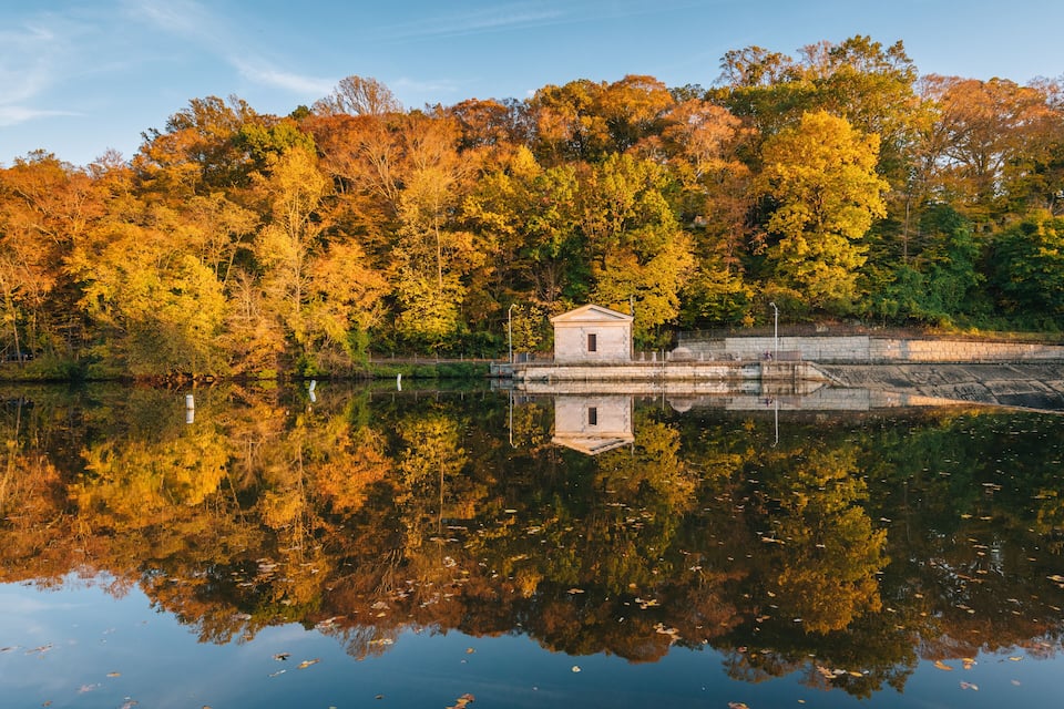 A small stone structure by a calm lake surrounded by autumn-colored trees.