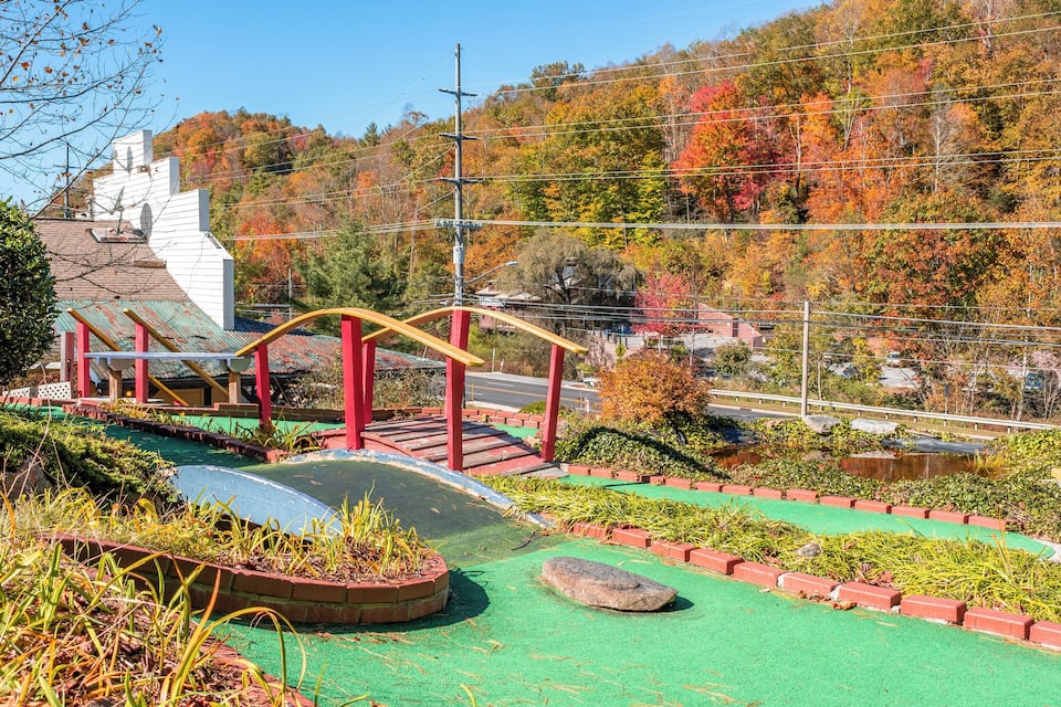 A park with a bridge, green pathways, and autumn trees.